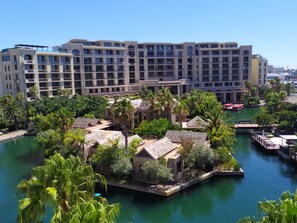 Un hôtel à étages, avec un plan d’eau au premier plan et une végétation luxuriante tout autour.