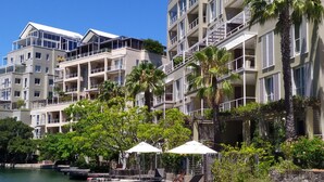 A waterfront hotel with multiple balconies, a swimming pool, and lush greenery.