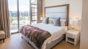 A hotel room with a large bed, a nightstand, a chair, and a view of buildings through the window.