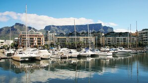 A marina with multiple boats docked, buildings with balconies, and a mountain in the background.
