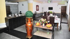 A hotel lobby with a reception desk, a large vase with a green top, and a dining area with tables and chairs. - Room-choice Gate Hotel-guest Suite (Benin City)