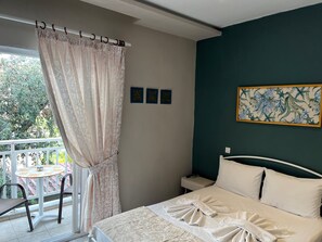 A bedroom with a bed, a nightstand, a chair, a table, and a view of greenery outside. - Room in Studio - Beautiful Room in Limenaria, Only Five Minutes Away From Center (Thasos)