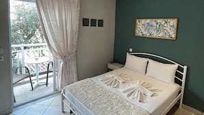 A bedroom with a bed, a bedside table, a chair, a curtain, and a balcony with a table. - Room in Studio - Beautiful Room in Limenaria, Only Five Minutes Away From Center (Thasos)