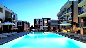 A swimming pool with lounge chairs and umbrellas, surrounded by multi-story buildings with balconies and air conditioning units. - Sunny Beach Retreat - 2-bedroom Apartment (Sunny Beach)
