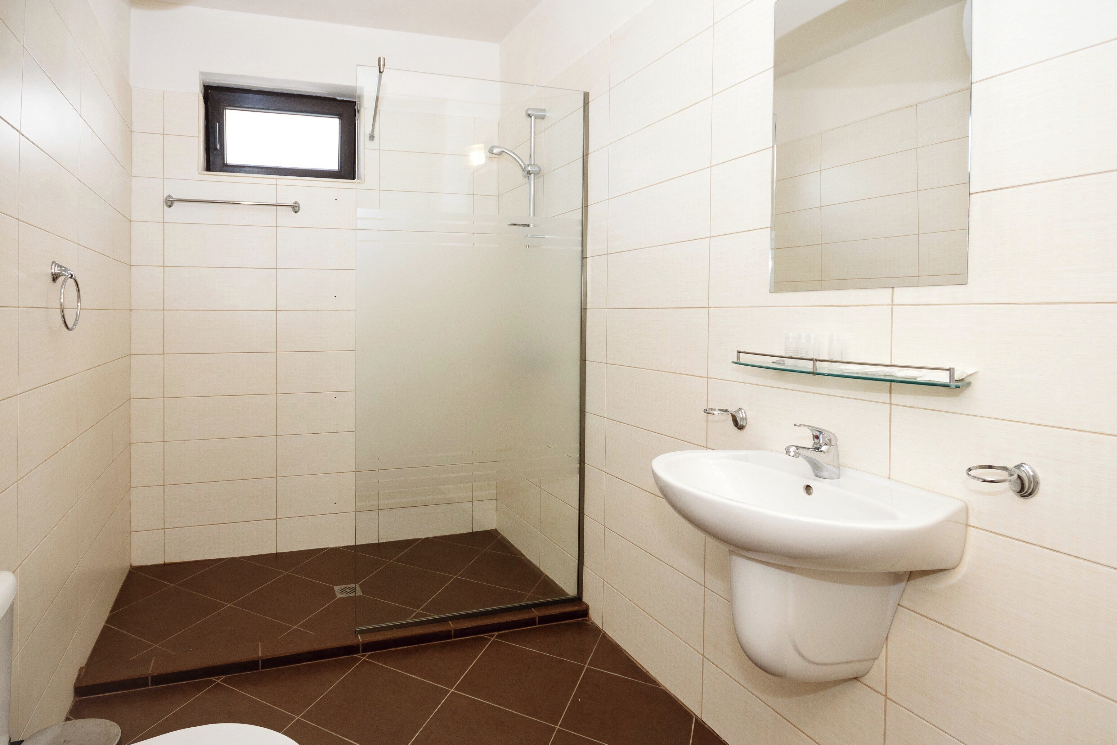 A bathroom with a shower, toilet, sink, and a small window.