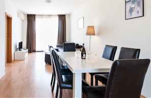 Ein Hotelzimmer mit Essbereich, ausgestattet mit einem weißen Tisch, schwarzen Stühlen, einer Lampe und einer Weinflasche.