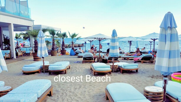 A beach with lounge chairs and umbrellas, a building with a balcony, and the ocean in the background. - Sunny Beach Retreat - 2-bedroom Apartment (Sunny Beach)