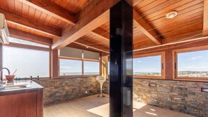 A spacious kitchen with a stone backsplash, wooden ceiling beams, and large windows offering a view of the landscape. - Masia Blanca by Interhome (Coma-ruga)