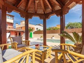 A covered outdoor seating area with wicker furniture, a pool, and a view of surrounding buildings.