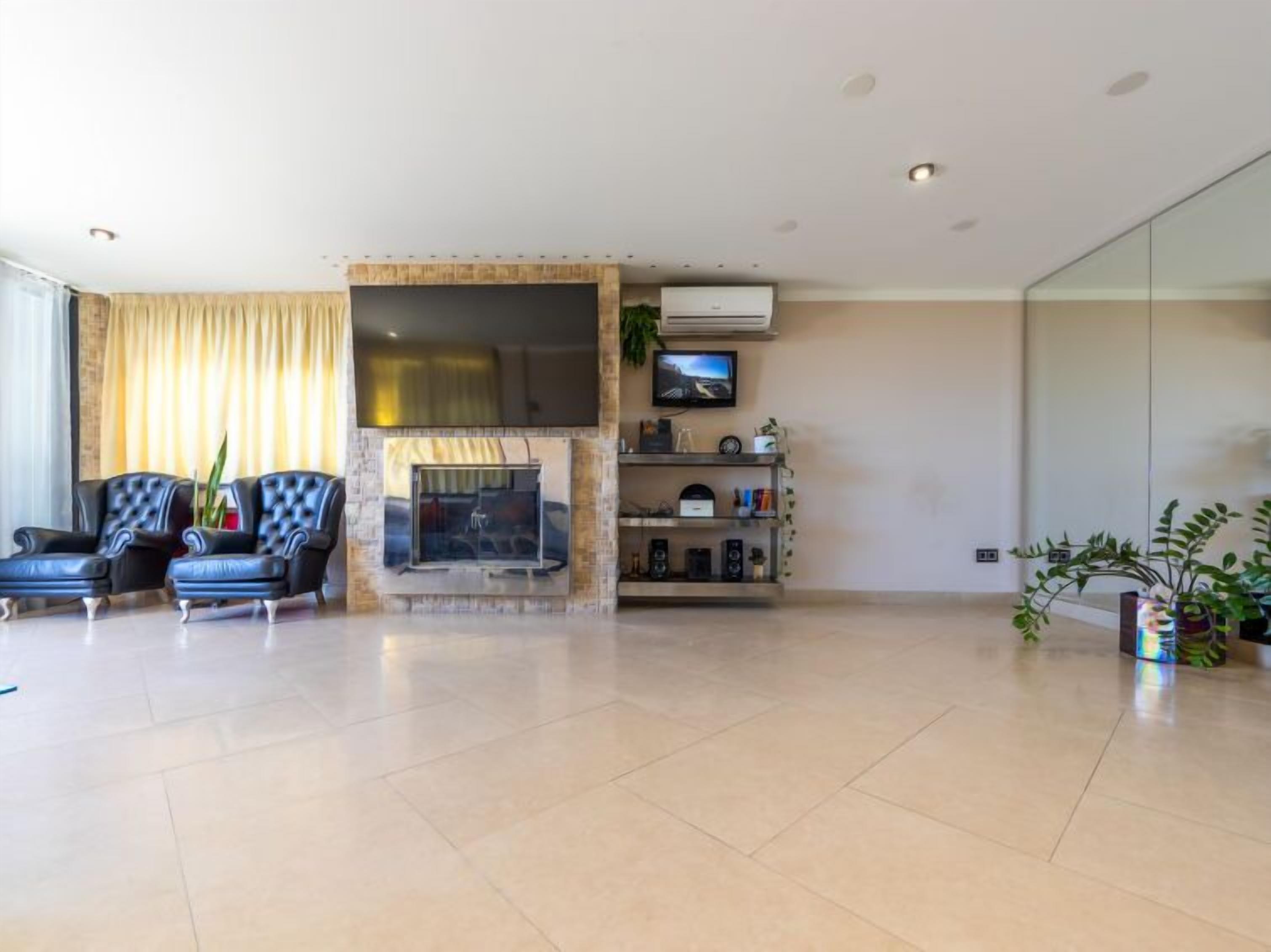 A modern living room with a fireplace, two leather armchairs, a television, and a glass partition wall.