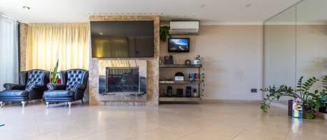 A modern living room with a fireplace, two leather armchairs, a television, and a glass partition wall.