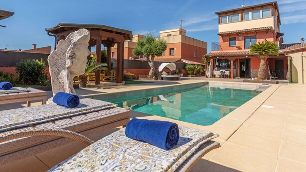A pool area with lounge chairs, a pergola, and a building with a balcony. - Masia Blanca by Interhome (Coma-ruga)