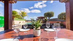 An outdoor dining area with a table set for four, a potted plant, and a view of a pool and garden. - Masia Blanca by Interhome (Coma-ruga)