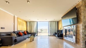 A spacious living room with a large flat-screen TV mounted on a stone wall, a comfortable sofa with cushions, and a glass coffee table. - Masia Blanca by Interhome (Coma-ruga)