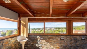 A room with a stone wall, a bar stool, and large windows offering a view of a town and sea. - Masia Blanca by Interhome (Coma-ruga)