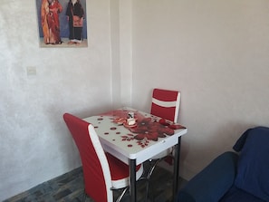 A small dining area with a table and two chairs, a painting on the wall, and a sofa in the corner.