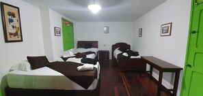 A hotel room with two beds, a wooden dresser, a green door, and a framed picture on the wall.