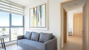 A modern living room with a grey sofa, a large abstract painting, and a view through a large window. - Minerva Zone Apartment Super Vista Fully Equipped Pool 3 Rec 6pp tv Wifi Aa (Guadalajara)