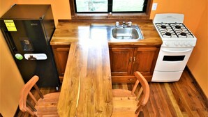 A compact kitchen with a wooden table, two chairs, a black refrigerator, a white stove, and a stainless steel sink. - Private 2-bedroom Jungle Cabin in Tropical Garden, San Ignacio (San Ignacio)