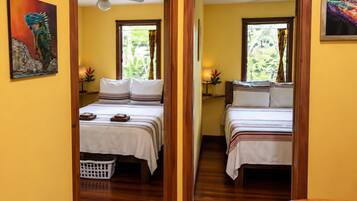 A hotel room with two beds, wooden flooring, a ceiling fan, and a window with curtains.
