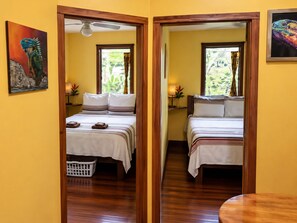 Habitación de hotel con dos camas, suelo de madera, ventilador de techo y ventana con cortinas.