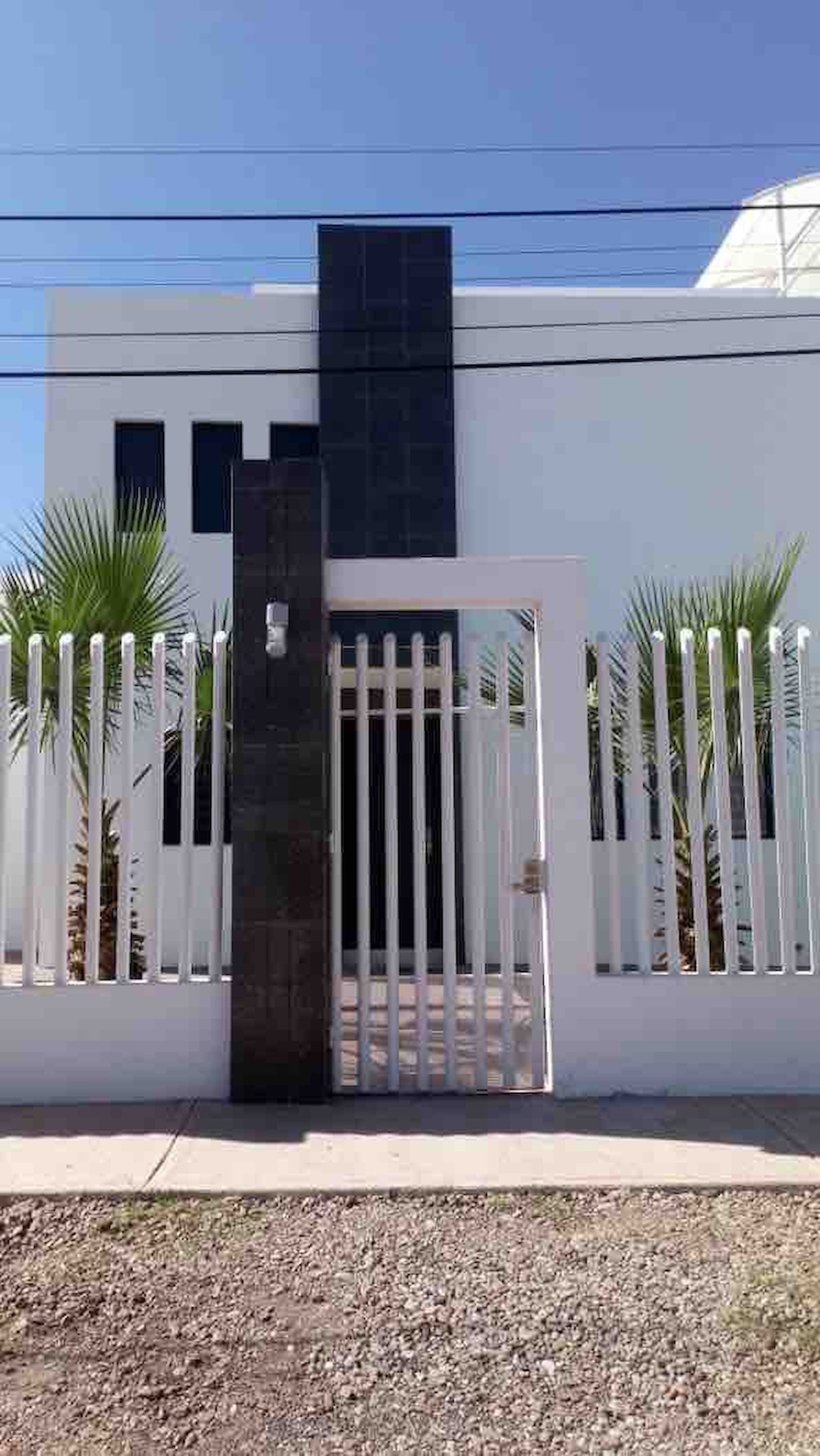 A modern building with a white exterior, a central black section, and a gated entrance.