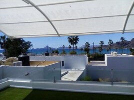 Una terraza en la azotea con toldo blanco, piscina y vistas al mar y las montañas.