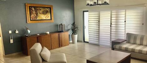 A living room with a sofa, armchair, coffee table, cabinet, and a painting on the wall.