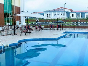 A swimming pool with lounge chairs and umbrellas, a fence, and a building labeled "AYIWOBU CONFERENCE CENTRE" in the background.