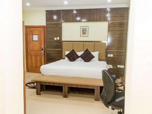 A hotel room with a large bed, a wooden bench, a desk, and a door. - Best Western Plus Mydas Hotel (Owo)