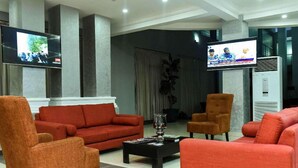 A modern lobby with red sofas, a coffee table, and two flat-screen TVs mounted on the walls. - Best Western Plus Mydas Hotel (Owo)