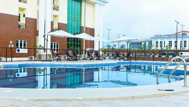A swimming pool with lounge chairs and umbrellas, a building with a large glass window, and a sign for the Aylwin Conference Center. - Best Western Plus Mydas Hotel (Owo)