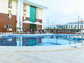 A swimming pool with lounge chairs and umbrellas, a building with a large glass window, and a sign for the Aylwin Conference Center. - Best Western Plus Mydas Hotel (Owo)