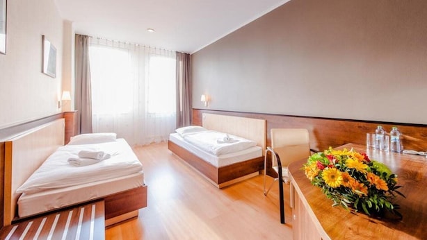 A hotel room with two beds, a wooden desk, and a vase of flowers. - Centrum (Kosice)