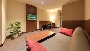 A hotel room with a sofa, a small desk, a television, and a potted plant. - Centrum (Kosice)