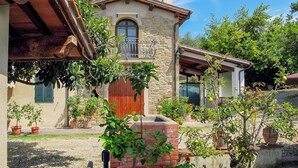A stone building with a wooden balcony, surrounded by potted plants and a gravel driveway. - Cosy apartment in villa for 3 guests with pool, WIFI, TV and patio (Castelfranco Di Sopra)