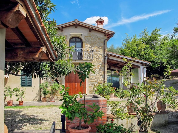 Un bâtiment en pierre doté d’un balcon en bois, entouré de plantes en pot et bordé d’une allée gravillonnée.