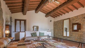 A cozy bedroom with a wooden ceiling, a stone wall, a bed with a quilt, a nightstand, and a window with curtains. - Cosy apartment in villa for 3 guests with pool, WIFI, TV and patio (Castelfranco Di Sopra)