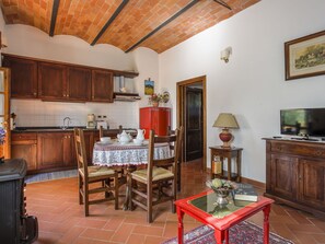 A cozy kitchen with wooden cabinets, a dining table with chairs, a red refrigerator, and a television on a wooden cabinet.
