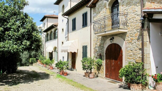 A row of traditional stone buildings with arched doorways, potted plants, and a cobblestone path.