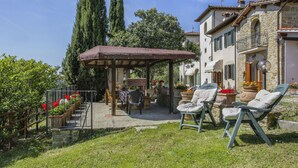 A covered outdoor seating area with a table and chairs, surrounded by potted plants and flowers.