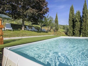 Une piscine à l’eau claire, entourée d’une pelouse avec des arbres et une structure en bois.