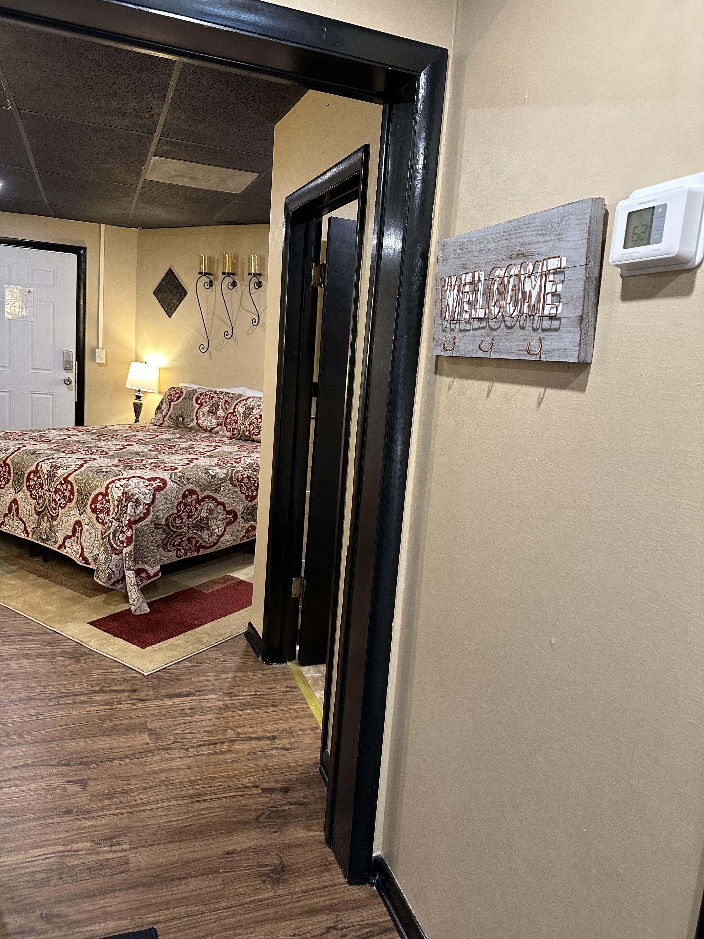 A hotel room with a bed, a welcome sign, a thermostat, and a lamp.