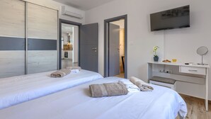Habitación de hotel con dos camas, televisión, escritorio con espejo y baño visible a través de una puerta abierta.