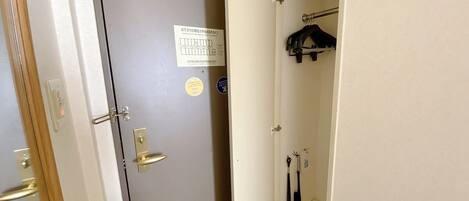 A narrow hallway with a door on the left and a closet with hanging items on the right.