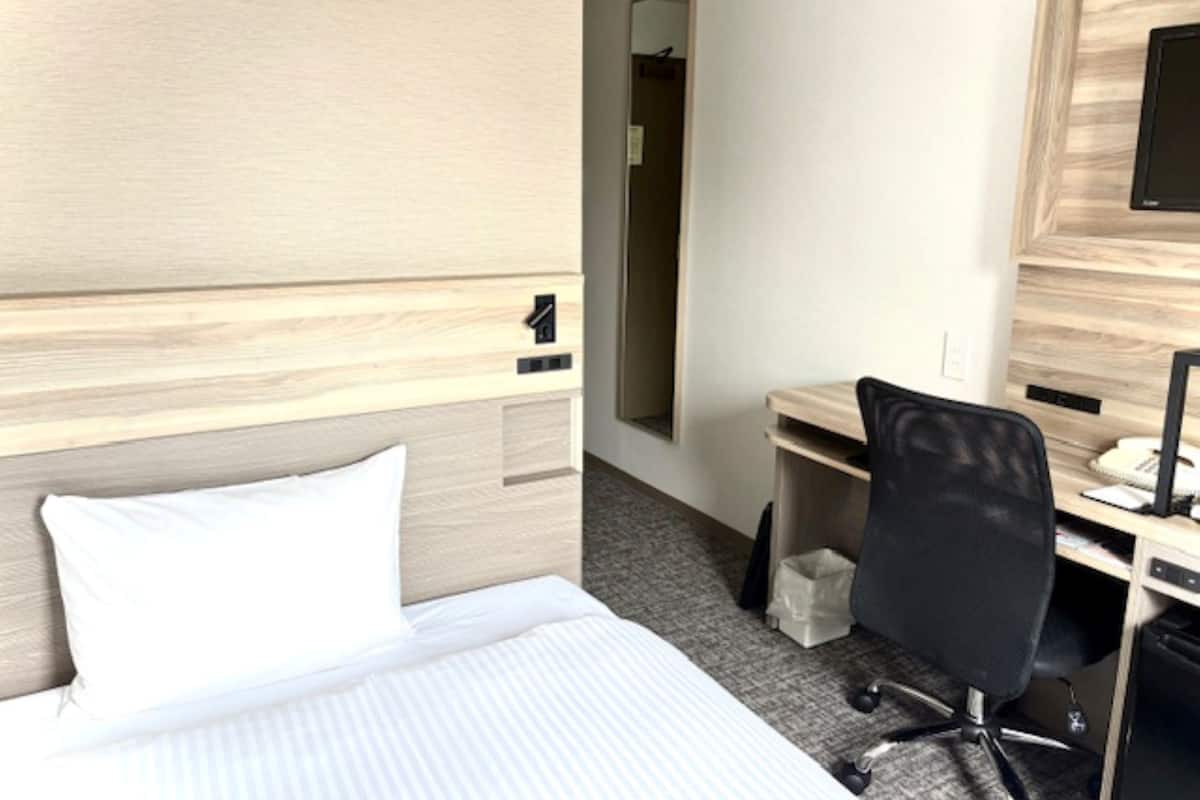 Una habitación de hotel con cama, escritorio, silla y ordenador.