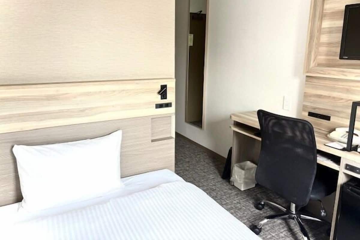 Una habitación de hotel con cama, escritorio, silla y espejo.