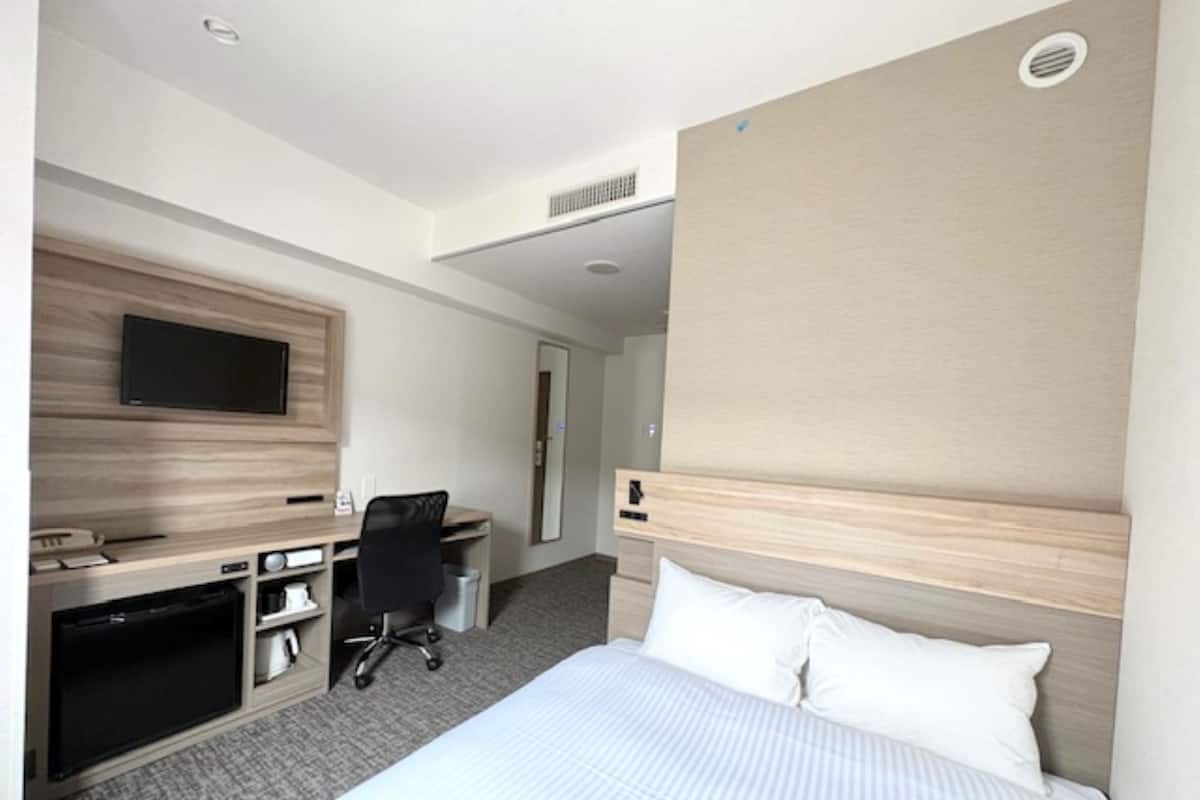 Una habitación de hotel con cama, escritorio, silla, televisor y puerta.