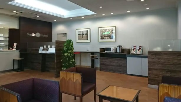 A hotel reception area with a reception desk, framed pictures on the wall, a small plant, and seating arrangements. - Smile Hotel Kitaasaka (Asaka)