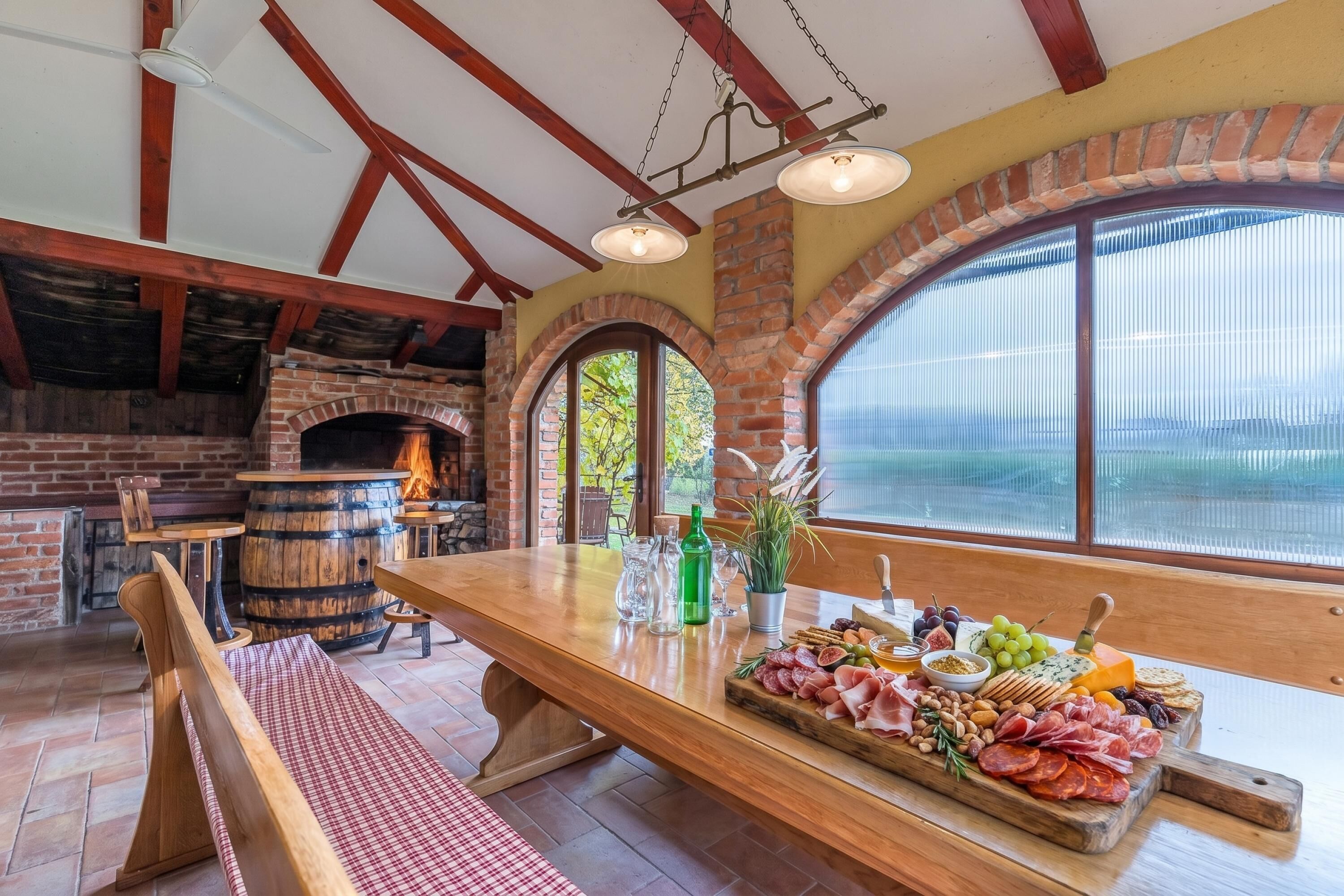 Un coin repas rustique avec une table en bois, une cheminée en briques et une grande fenêtre en arc de cercle.